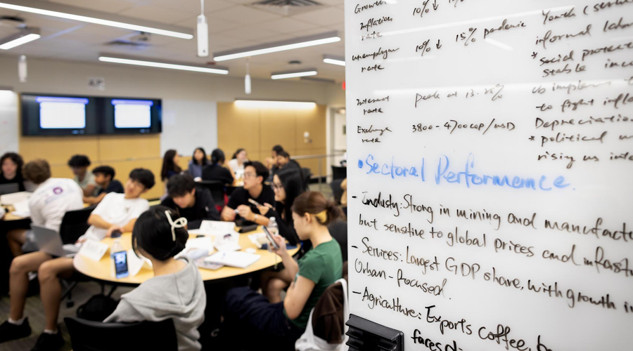 Economics Academy students work on a game theory project with notes from a previous international research project on the whiteboards.